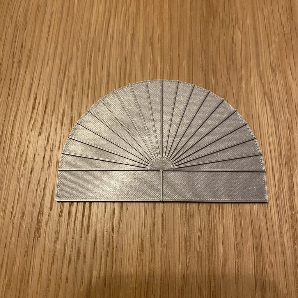 kątomierz pomiarowy, PLA srebrne Srebrny kątomierz pomiarowy w formie półkola ze zbiegającymi się liniami. Oznaczone są kąty co 10 stopni.