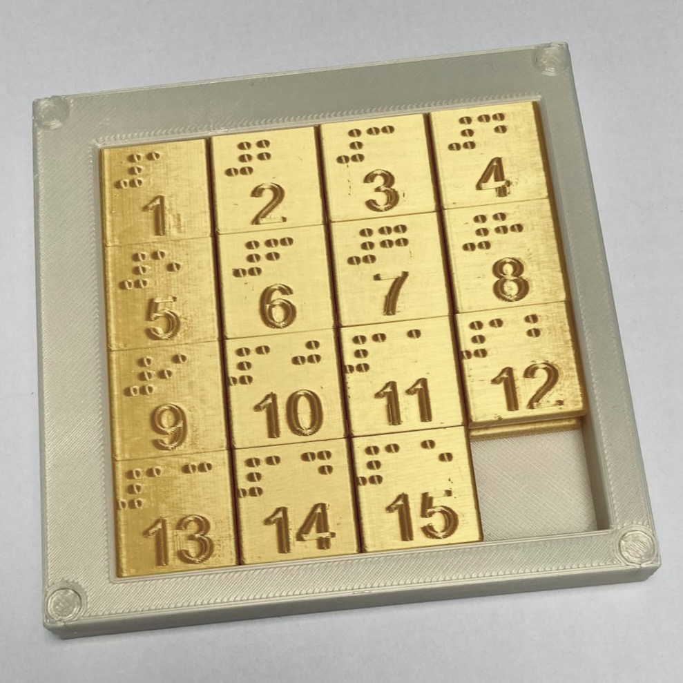 Piętnastka Piętnastka: ujęcie lekko pod kątem, dzięki czemu widać wszystkie elementy. Na elementach brajlowskie i czarnodrukowe liczby od 1 do 15.