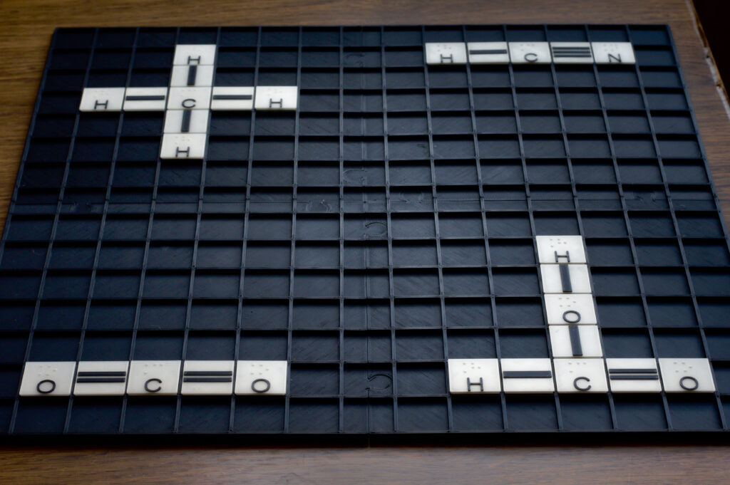 Tablica do układania wzorów strukturalnych Na tablicy ułożone są cztery przykładowe wzory strukturalne. Kolejnymi ćwiartkami układu współrzędnych są to: cyjanowodór (HCN), metan (CH4), dwutlenek węgla (CO2) i kwas azotowy (HNO3).