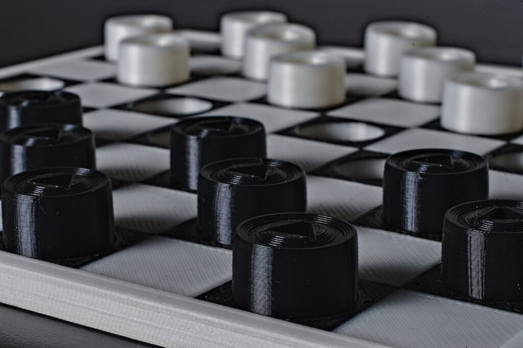 Warcaby, rzut prostopadły Warcabnica z ustawionymi pionkami, naprzemiennie znajdują się czarne (wklęsłe) i białe (płaskie) pola.