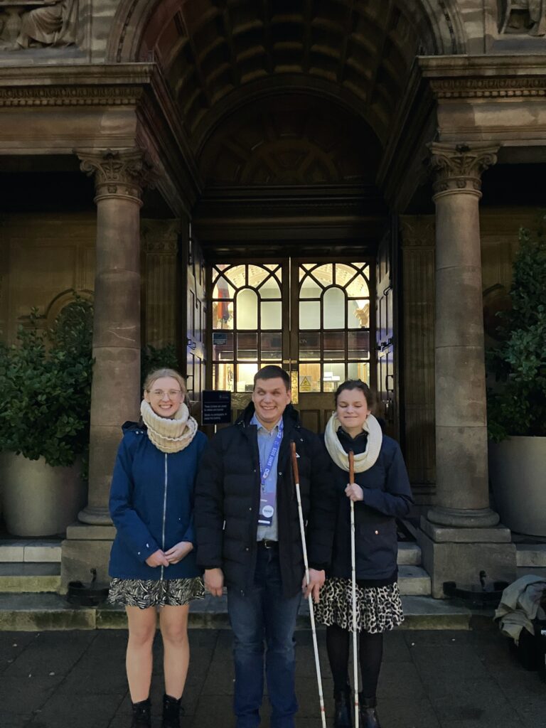 Dawid, Julita i Magda stoją na progu zabytkowego budynku. Widać zieleń przy schodach i ornamenty na ścianach