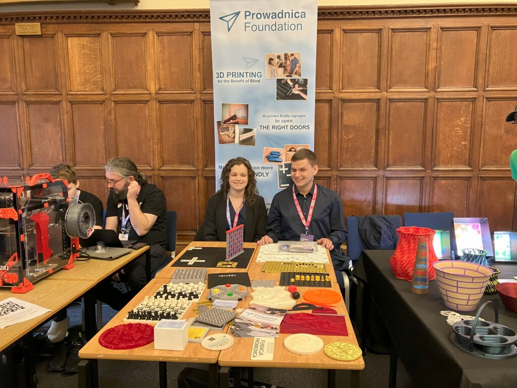 Dawid i Julita przy swoim stanowisku. Widać baner fundacji, stół z wydrukami i inne stanowiska