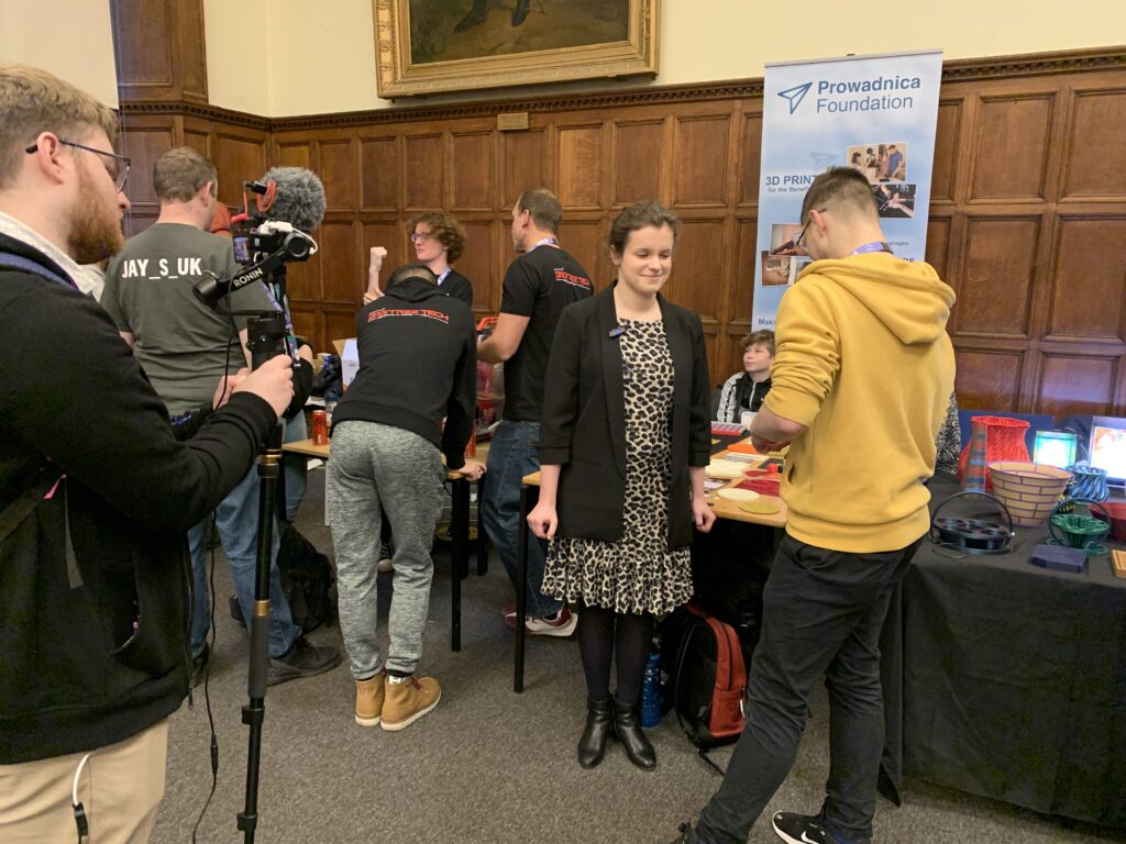 Dużo ludzi stoi przy stanowisku fundacji. Julita rozmawia z prezenterem telewizyjnym, wszystko nagrywa kamerzysta