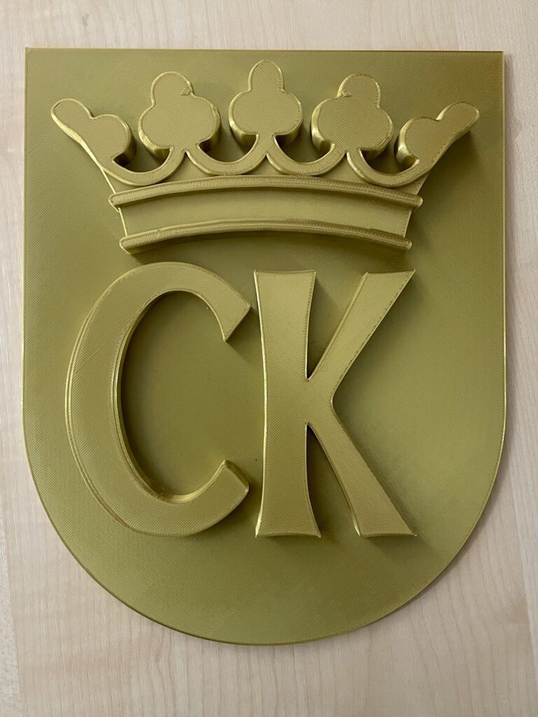 Herb Kielc Na dole tarczy znajdują się duże litery CK. Nad nimi korona z pięcioma trójlistnymi kwiatami.